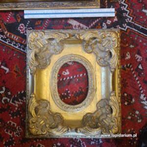 Masywna, zabytkowa rama dekoracyjna wykonana z drewna i gipsu na białym tle.