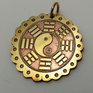 Ręcznie wykonany amulet z mosiądzu z symbolem Yin-Yang i ośmioma triagramami I-Cing na okrągłej podstawie.
