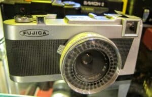 Kolekcjonerski, czarny aparat fotograficzny Fujica Rapid z lat 60. z automatycznym naciągiem filmu, widok z przodu.