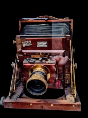 Antyczny, drewniano-mosiężny aparat fotograficzny Senderson London z XIX wieku na tle ciemnego sukna.