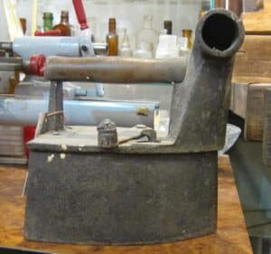 Dawne żeliwne żelazko z charakterystycznym wysokim kominem na węgiel drzewny, antyk z przełomu XIX i XX wieku.