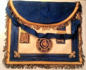 Antyczny biały fartuszek masoński z Loży Walijskiej w komplecie z dwoma mankietami na ciemnym tle.