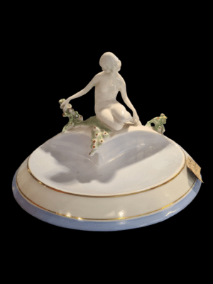 Porcelanowa figurka nago siedzącej kobiety z rośliną na postumencie z reliefowymi dekoracjami kaktusów