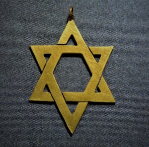 Ręcznie wycinana mosiężna Gwiazda Dawida, amulet z pracowni Mistrza Kilińskiego z XX wieku na tle.