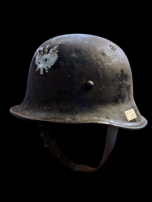 Hełm niemiecki stalowy M35 z okresu II wojny światowej z przymocowanym na przodzie metalowym polskim orłem.