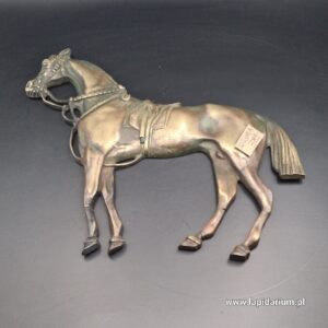 Mosiężna plakieta z reliefem przedstawiającym konia na tle patynowanego metalu.