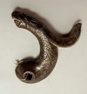 Ozdobny mosiężny kurek (szczęka kurkowa) z XVIII-wiecznej broni kapiszonowej na ciemnym tle.