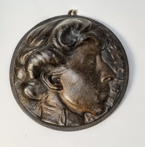 Plakieta kolekcjonerska z portretem Królowej Belgijskiej, metalowy odlew na ciemnym tle.