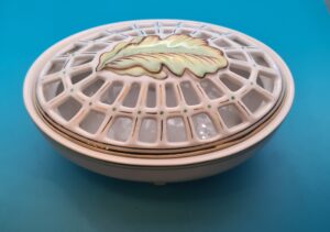 Porcelanowe białe naczynie z ażurowym, ozdobnym wieczkiem z okresu PRL na tle neutralnym.