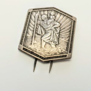 Srebrna spinka z wyraźnym wizerunkiem św. Krzysztofa, amulet ochronny dla podróżujących na białym tle