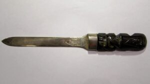 Srebrny nóż do papieru z rzeźbioną głową Aztecką z czarnego obsydianu na białym tle.