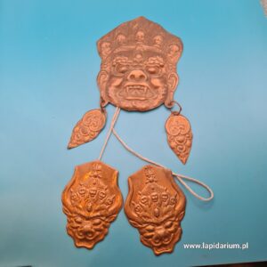 Trzy miedziane wisiorki z wizerunkami tybetańskich demonów-strażników (Dharmapala) z XX wieku na tle.