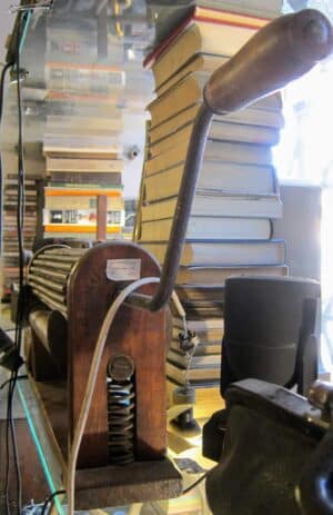 Zabytkowe, ręczne urządzenie do walcowania tytoniu z Kuby z lat 20. XX wieku na tle ciemnego drewna.